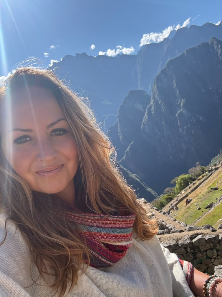 Sarah, founder of Truest Publishing Co., smiling in a woven scarf on a sunlit mountain trail with terraced ridges behind her